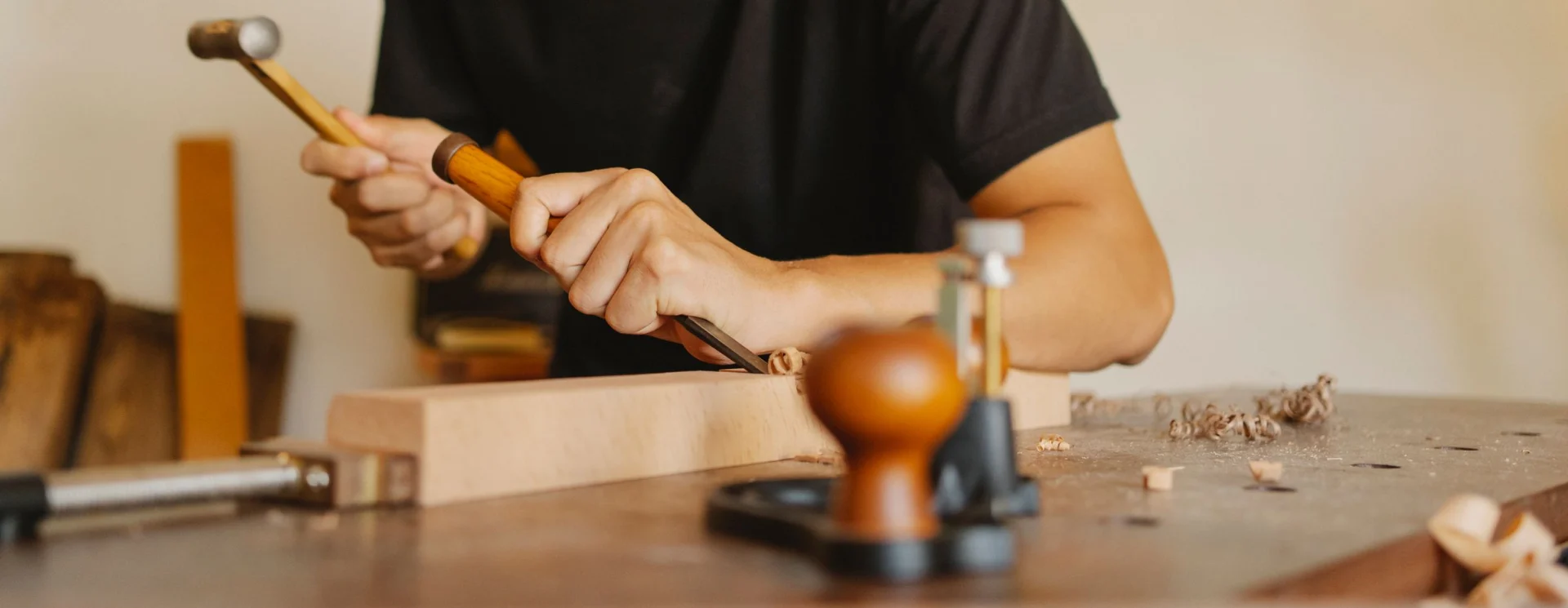A person carves wood with a chisel and mallet on a workbench in a workshop.