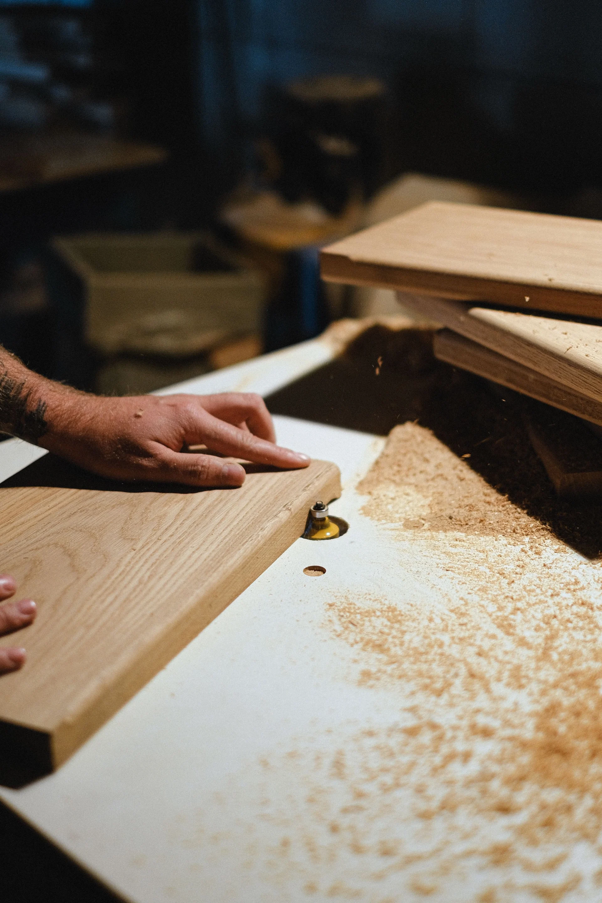 A person's hand guides a piece of wood through a woodworking machine in a workshop.