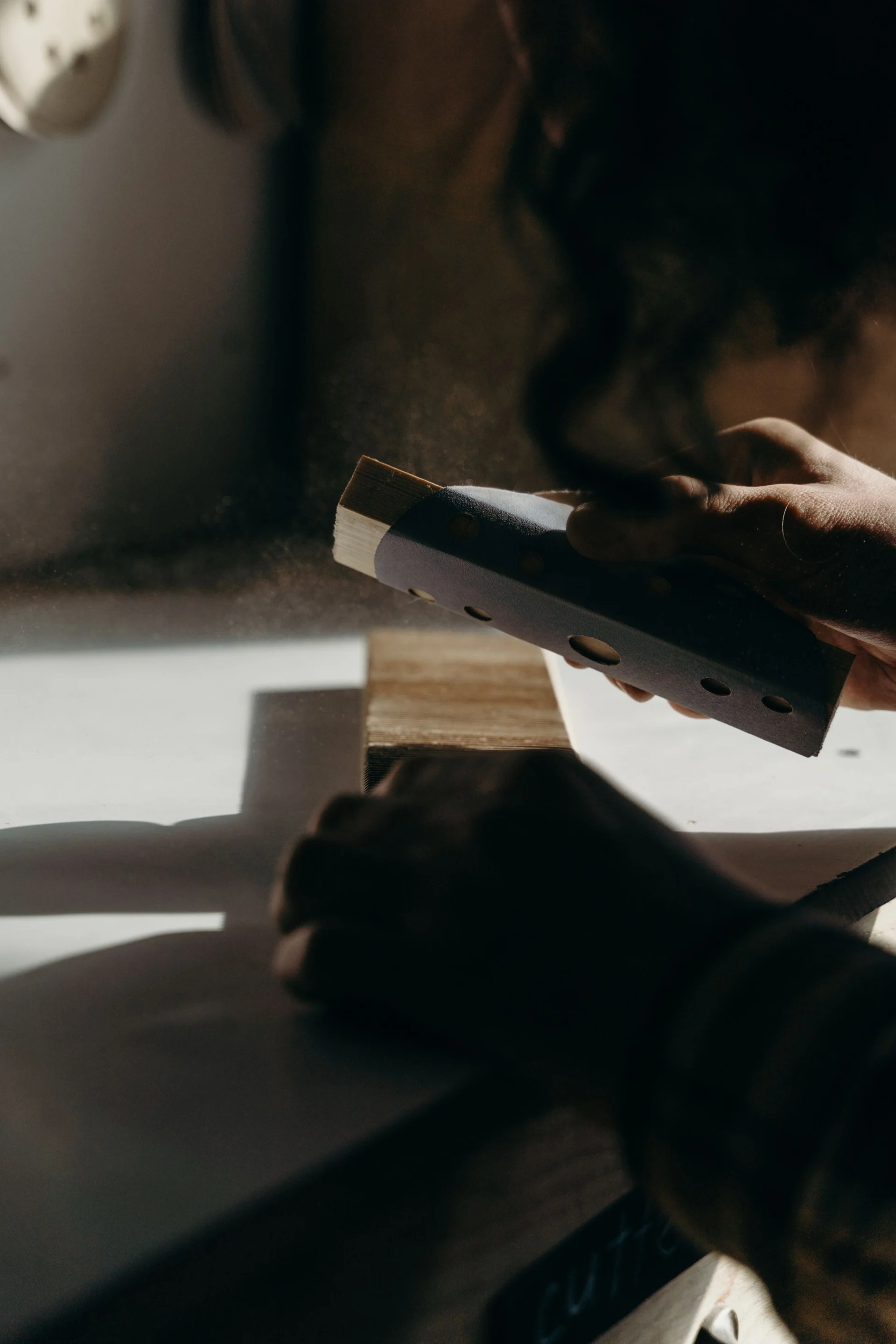 A person sanding a piece of wood with a sanding block on a work surface.